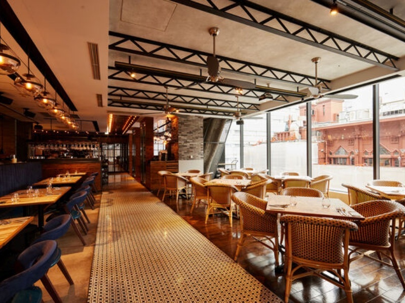 インダストリアルな天井とラタンチェアが調和したスタイリッシュな店内。大きな窓から望む景色とともに、特別なひとときをお過ごしください。
