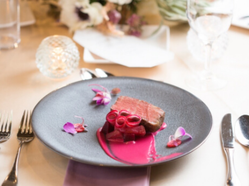 黒いプレートに鮮やかに盛り付けられた肉料理。赤いソースと花びらの装飾が芸術的な美しさを添える、EYOHAKUならではの創作フレンチです。